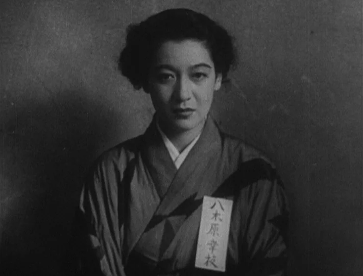 No Regrets for Our Youth (1946) movie still: medium — A woman stands centered against a flat, undifferentiated background wall. She wears a…