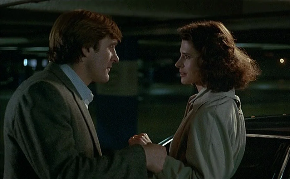 The Woman Next Door (1981) movie still: medium — A dimly lit concrete structure with support columns and distant ambient city lights. A man and a…