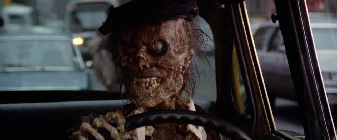 Ghostbusters (1984) movie still: medium — A decaying, skeletal creature sits in the driver seat of a car in traffic. The figure grips the steering…