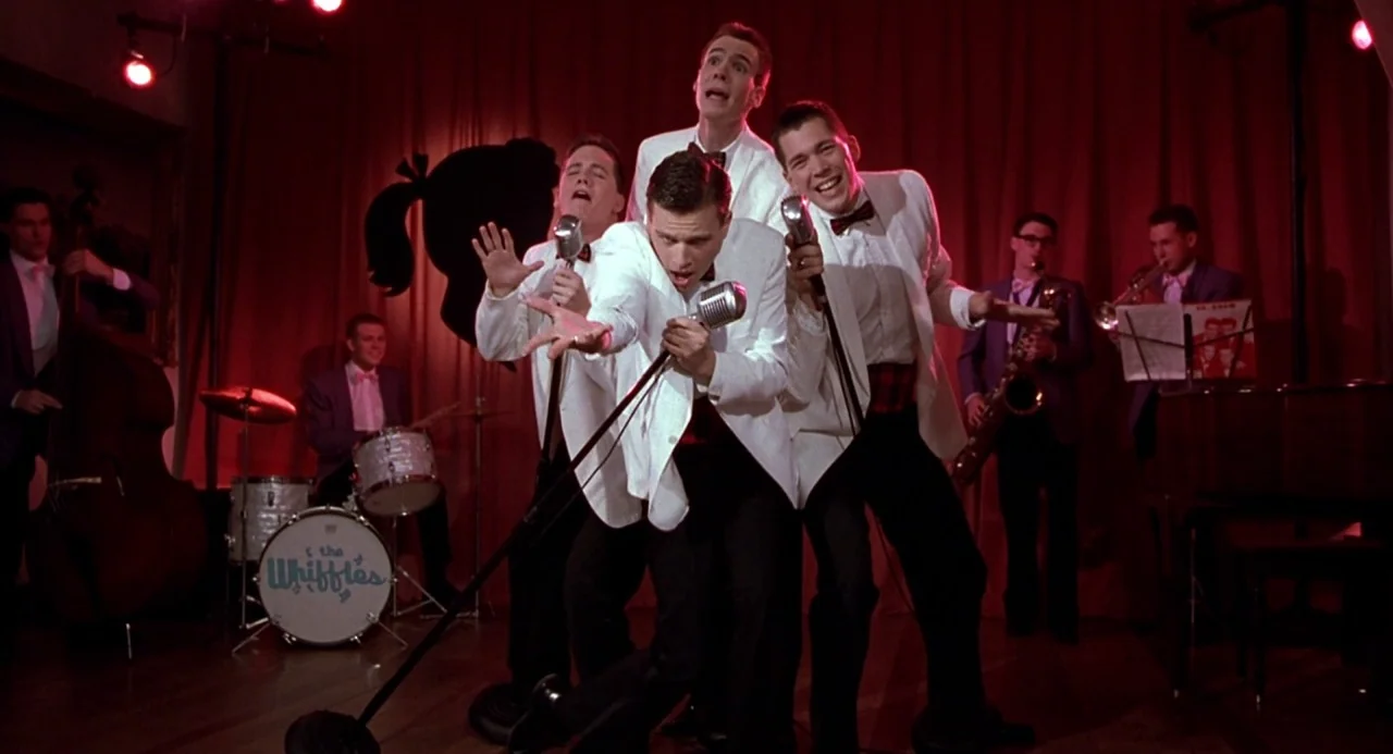 Cry Baby (1990) movie still: medium — A 1950s themed stage features a vocal quartet performing in front of red curtains. Musicians play instruments…