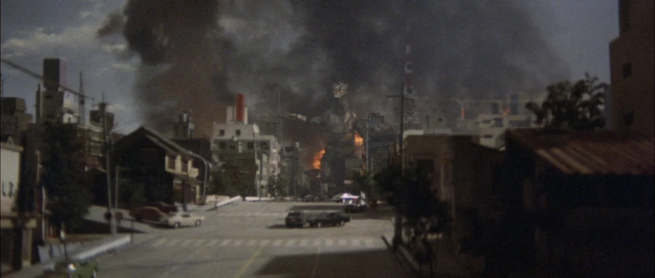 Terror of Mechagodzilla (1975) movie still: wide — An empty urban street at night with cars parked along the curb. A massive mechanical monster…