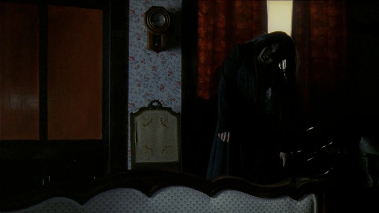 A Tale of Two Sisters (2003) movie still: medium — A dark parlor features flowered wallpaper and a wall-mounted wooden clock. A woman in a black…