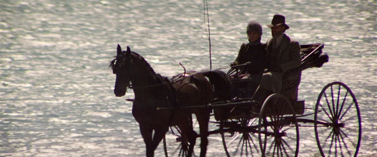 Heaven’s Gate (1980) movie still: wide — A horse pulls a carriage through shallow, reflective water in a broad landscape. The two passengers are…