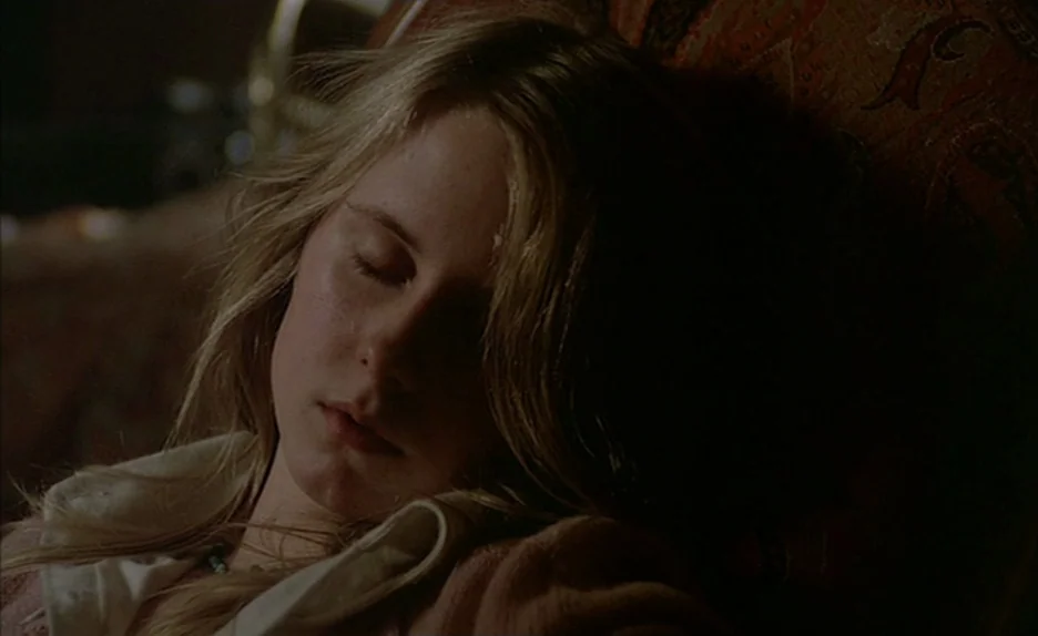 Black Moon (1975) movie still: closeup — A teenage girl rests her head against the back of an ornate patterned armchair. She appears to be asleep in…