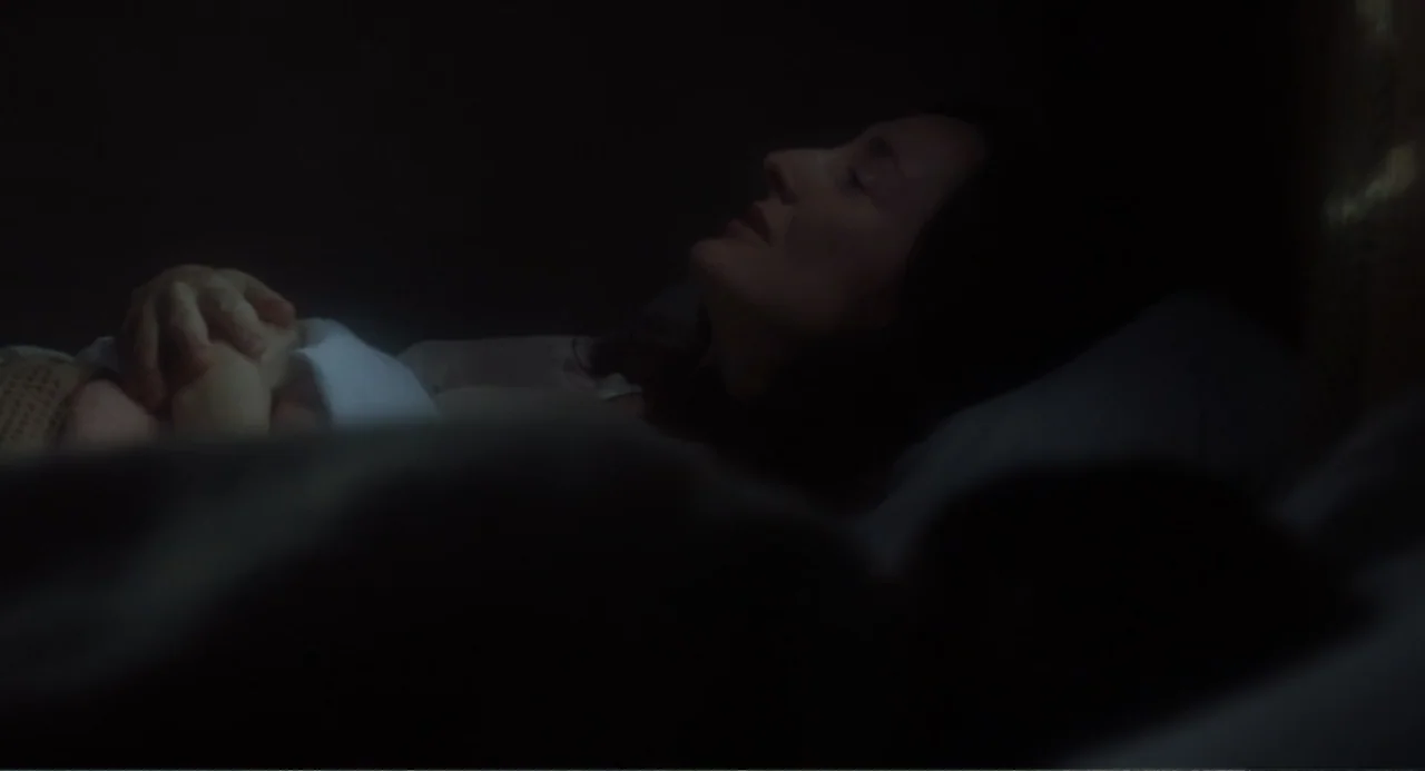 Dancing at Lughnasa (1998) movie still: closeup — A dark bedroom interior with a woman sleeping in a bed. The person lies on white pillows with eyes…