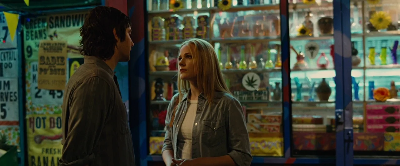 Across the Universe (2007) movie still: medium — The exterior of a cluttered shop at night features shelves full of glassware. A young man and woman…
