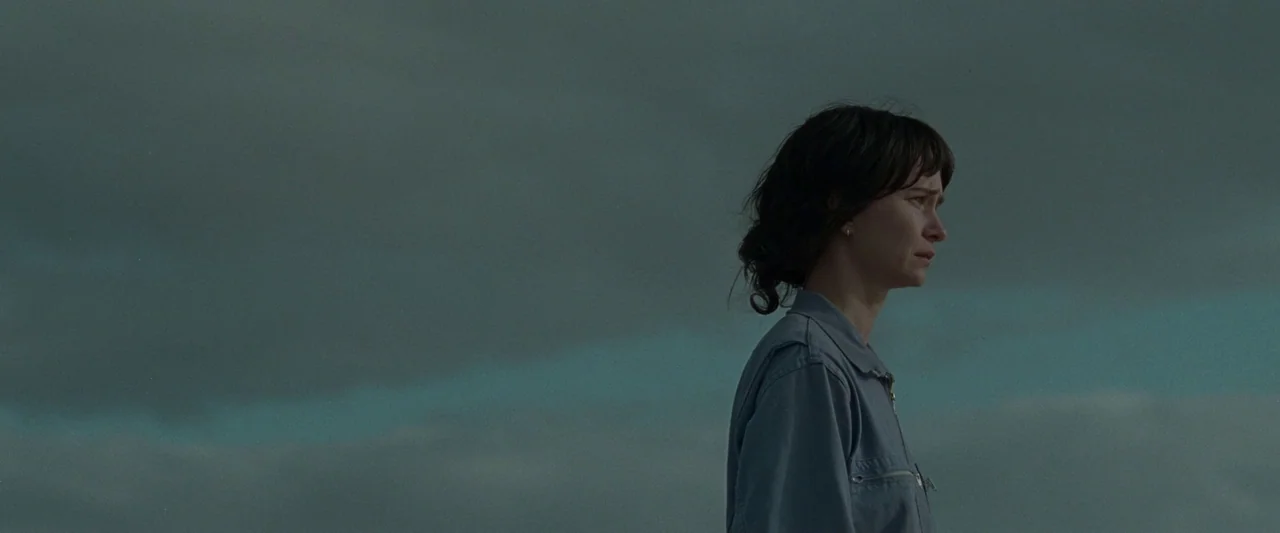 The End We Start From (2023) movie still: medium — An overcast sky hangs over a coastal landscape with limited visible environment detail. A woman…