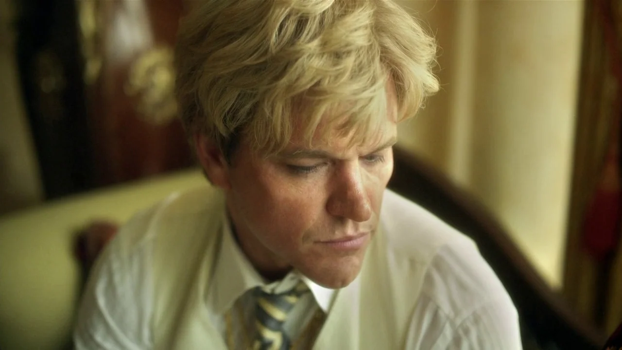 Behind the Candelabra (2013) movie still: closeup — An interior space features a person sitting in a dimly lit, plush setting. A man with blonde…