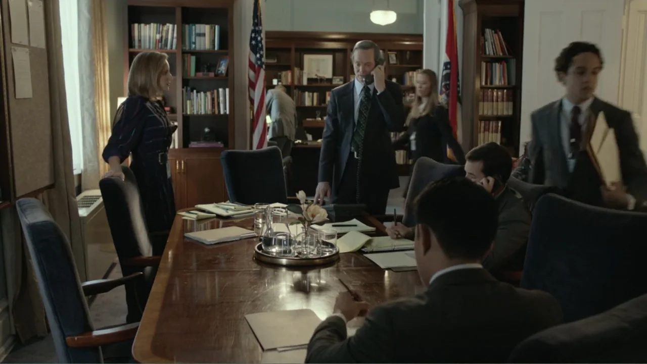 Confirmation (2016) movie still: medium — A professional office suite features bookshelves, American flags, and a large wooden central table. Staff…