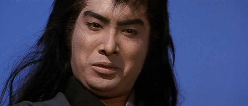 Lone Wolf and Cub: Baby Cart in Peril (1972) movie still: closeup — A man with long hair poses against a clear, solid blue sky background. The…