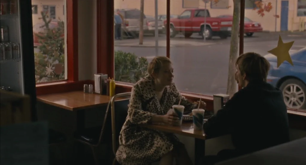 Restless (2011) movie still: medium — A diner booth faces a window looking out onto a parking lot. A woman and a man sit across from each other…