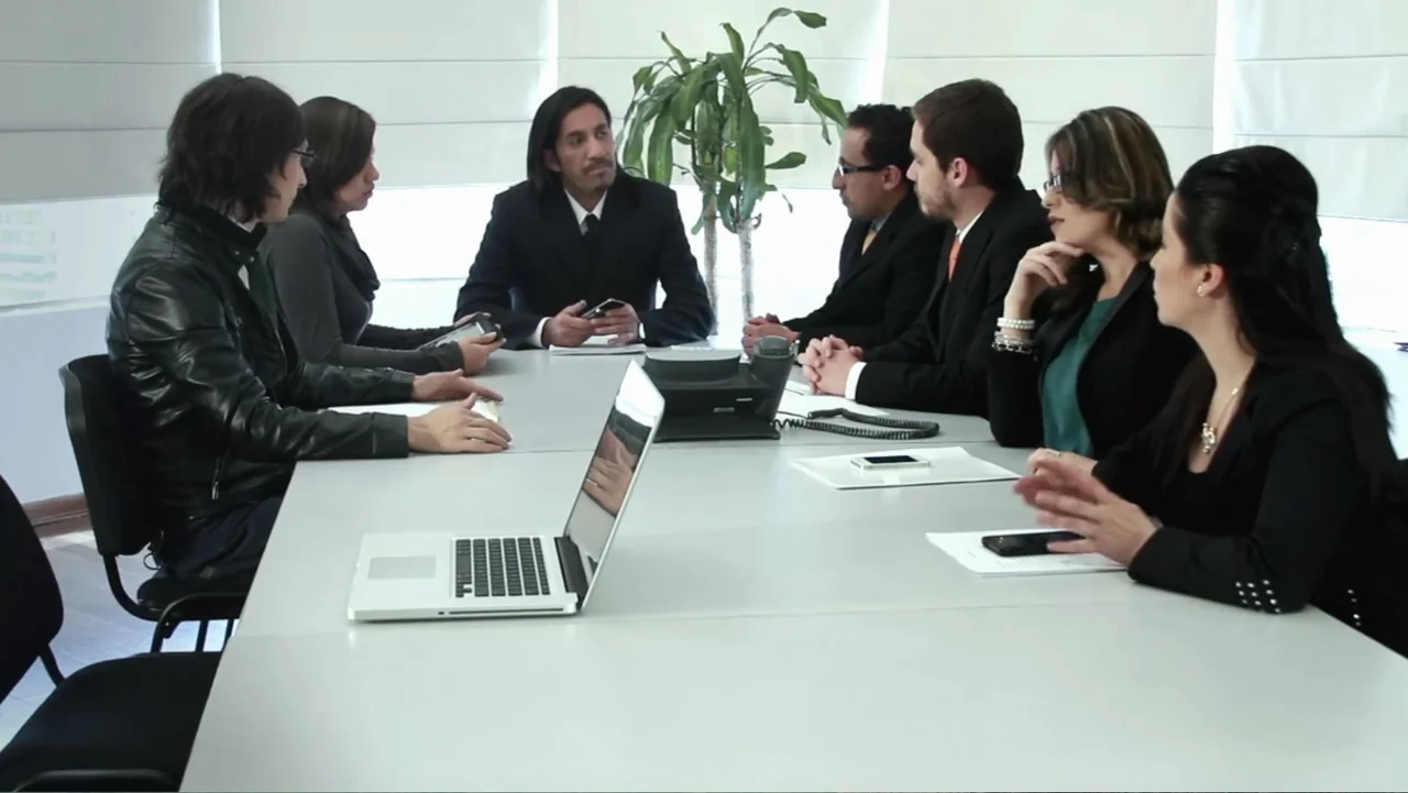 Aquel Septiembre (2018) movie still: medium — A bright modern office conference room features white walls with large window blinds. Seven business…
