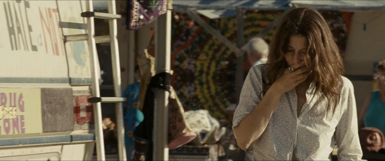 Into the Wild (2007) movie still: medium — An outdoor bazaar features a painted van and colorful fabric stalls in the background. A woman in a…