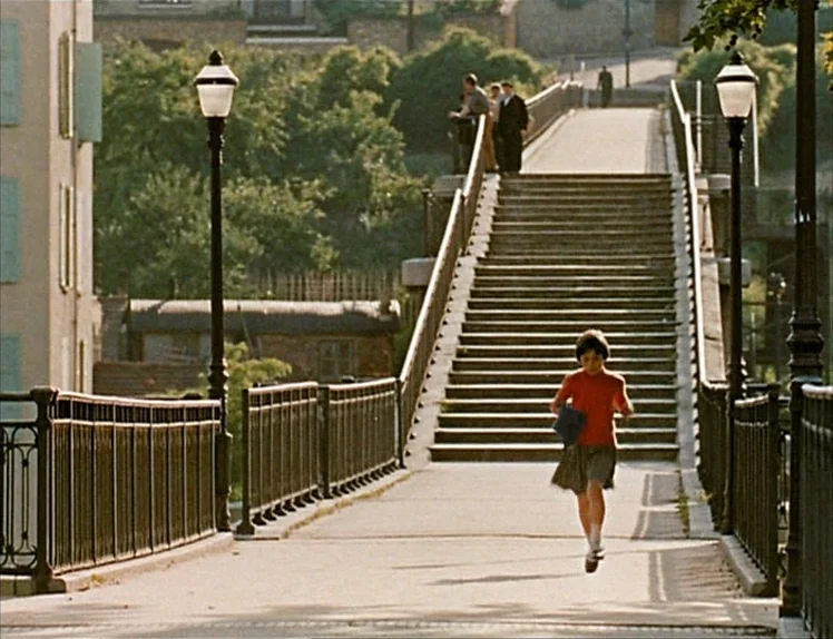 Zazie Dans Le Métro (1960) movie still: fullbody — A long pedestrian bridge with stairs leads upward toward a treelined embankment. A young girl in…