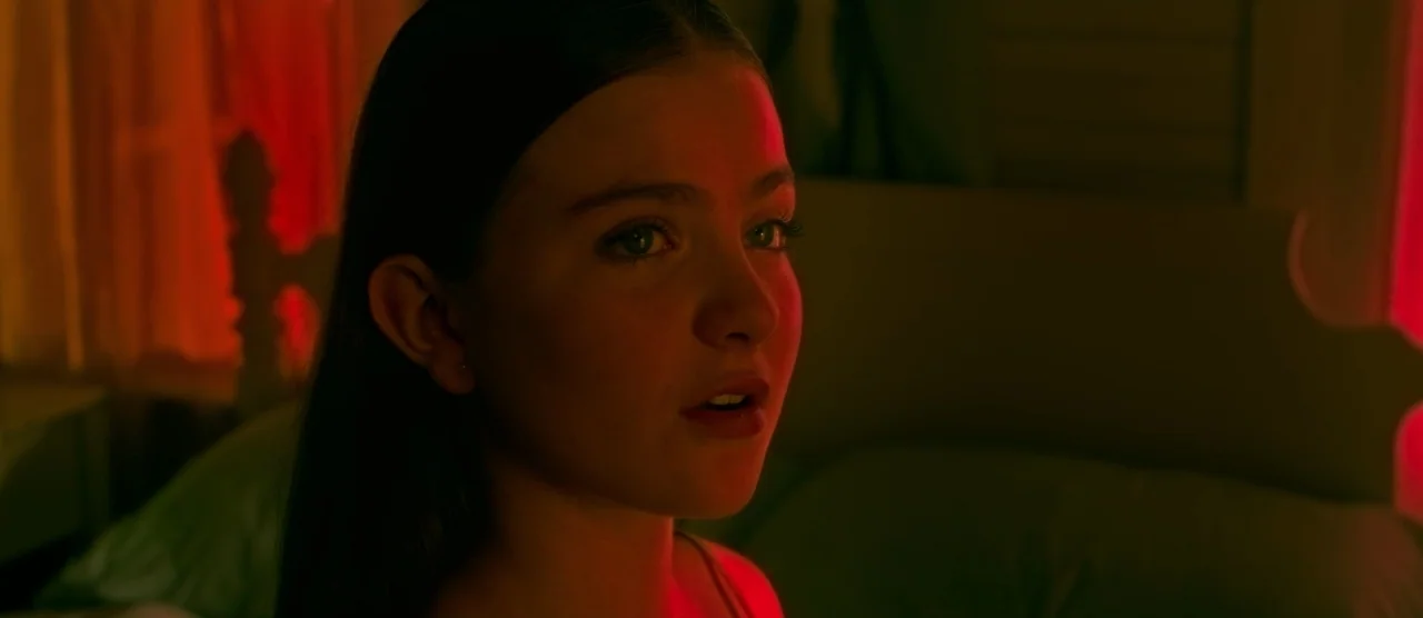 Gerald’s Game (2017) movie still: closeup — A dark room illuminated by a strong red light source. A teenage girl looks slightly off-camera with a…