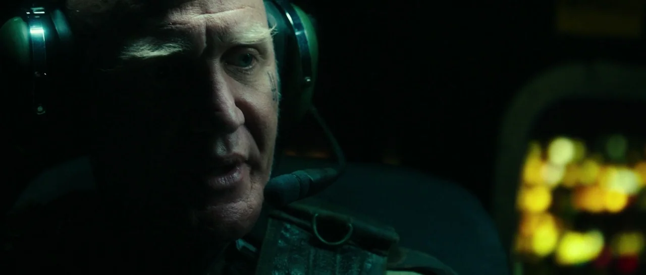 The Purge: Election Year (2016) movie still: closeup — A dimly lit pilot seat within a cockpit features an older man wearing headphones. The subject…