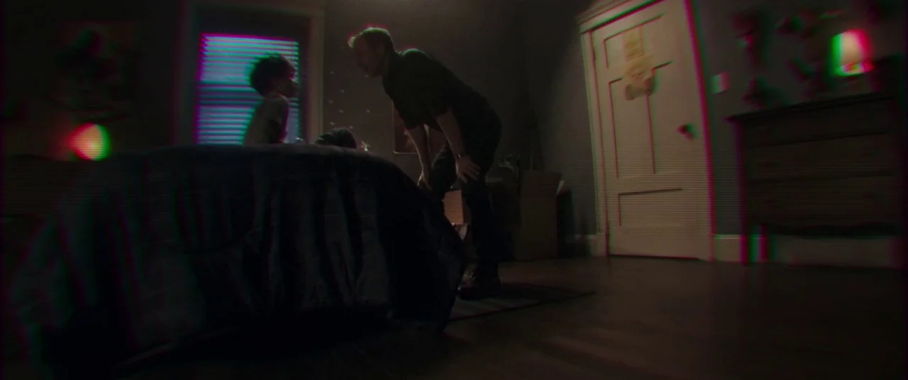 Child's Play (2019) movie still: wide — A dimly lit room contains a bed and a dresser against a wall. An adult male stands near the bed where a…