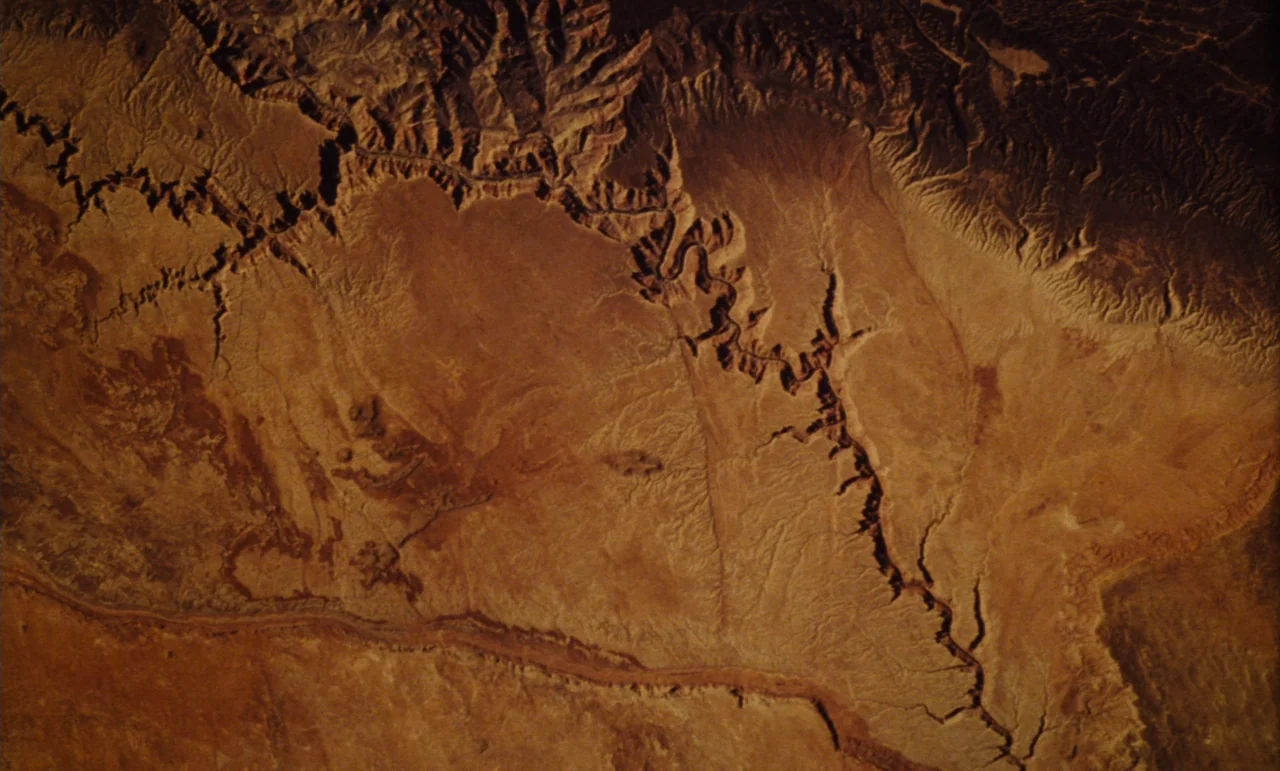 Until The End Of The World (1991) movie still: establishing — An aerial view shows a vast, dry desert landscape with deep winding river canyons.…