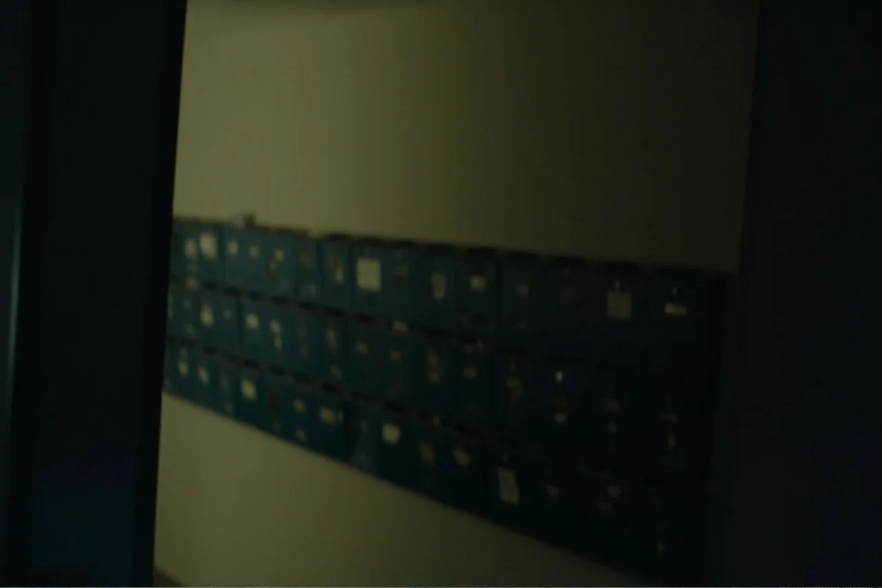 Cross the Line (2020) movie still: medium — A dimly lit interior wall features rows of metal mailboxes mounted on a surface. The scene is framed by…
