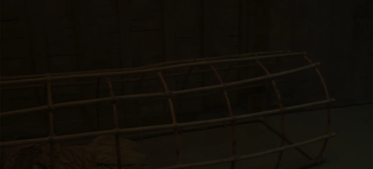 A Thousand Days (2023) movie still: medium — A dark, dimly lit room contains a hollow, arched wooden framework structure. Empty space surrounds the…