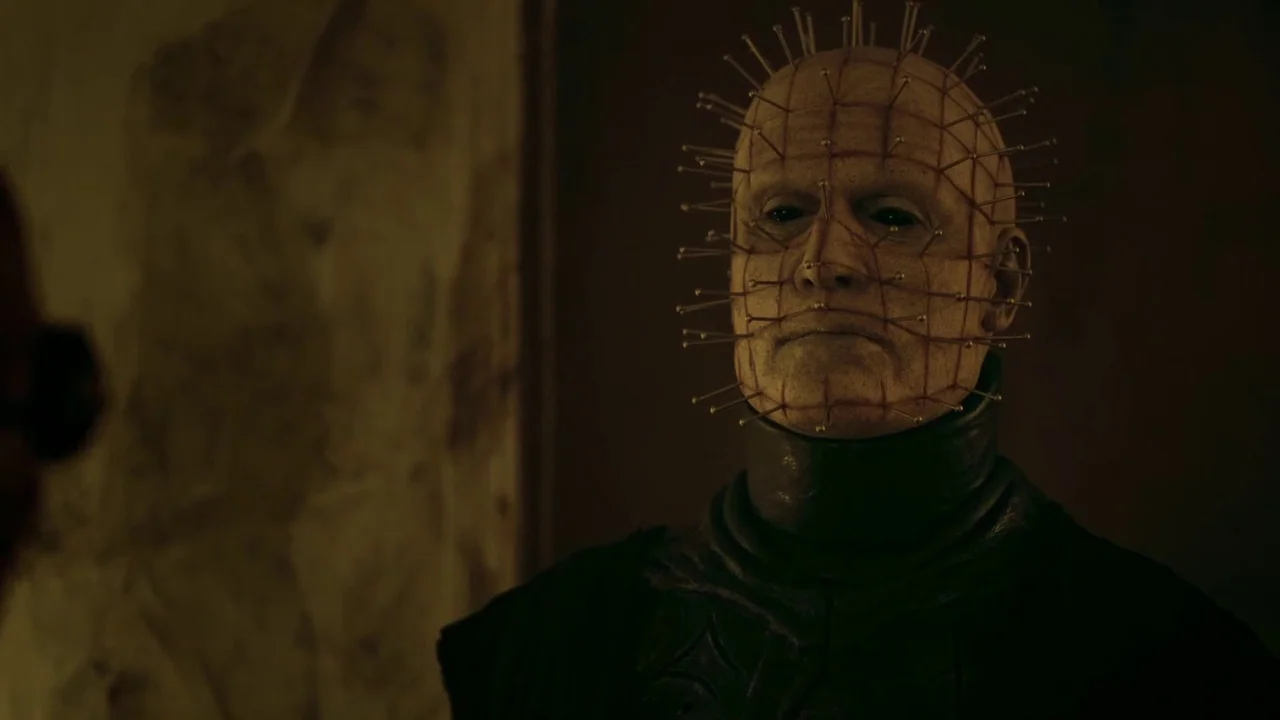 Hellraiser: Judgement (2018) movie still: closeup — A dark, dimly lit environment with textured walls visible behind the subject. A pale,…