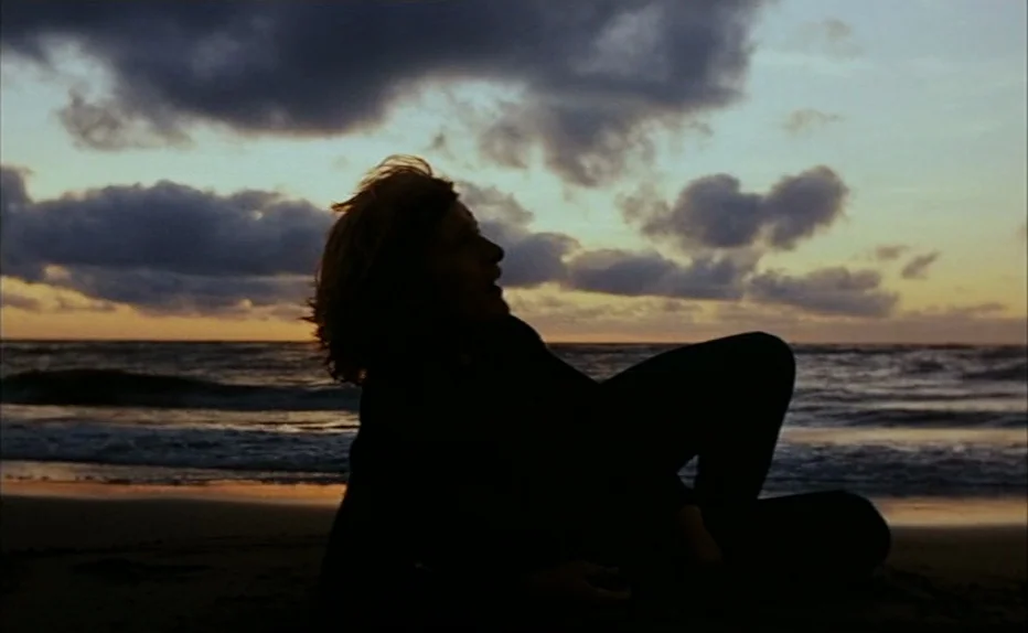 Turkish Delight (1973) movie still: medium — A dark sandy shoreline sits under a sky filled with layered, textured evening clouds. A person in dark…