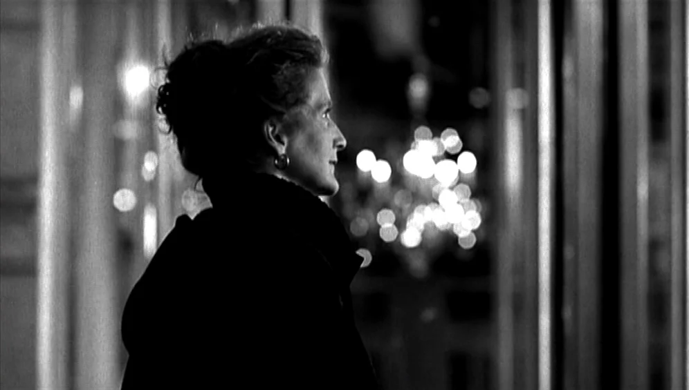 The Tango Lesson (1997) movie still: medium — An urban setting at night featuring a woman standing before a backdrop of bokeh. The woman observes…