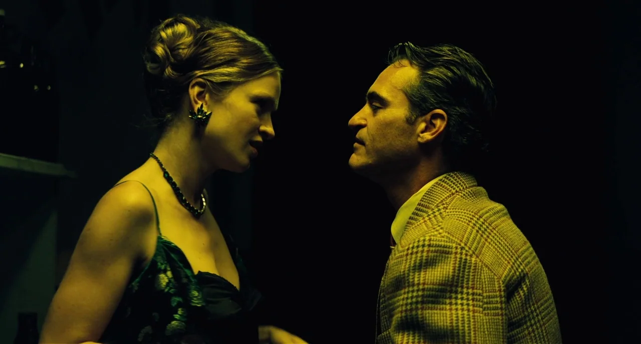 The Master (2012) movie still: medium — A dark room with minimal architectural detail visible in the heavy shadows. A man in a patterned blazer…