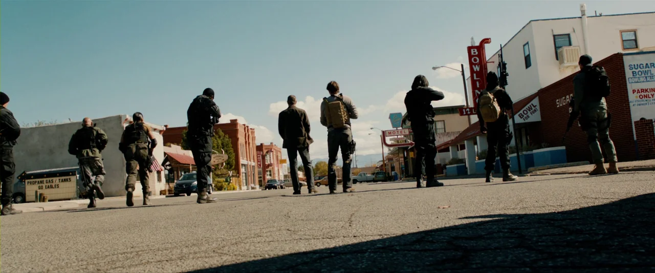 The Last Stand (2013) movie still: A tactical team walks in formation across a deserted small-town street, captured from a low, wide perspective.…