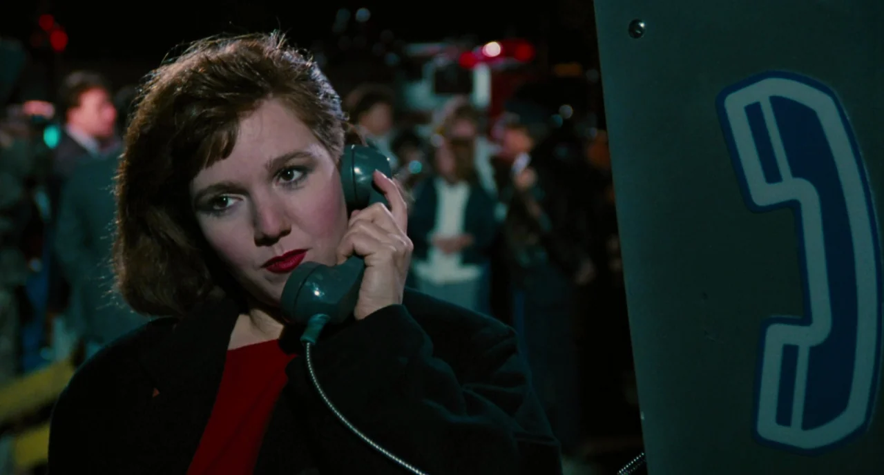 The Big Easy (1986) movie still: A young woman stands in a crowded, dark urban street at night, isolated by the camera's shallow depth of field as…