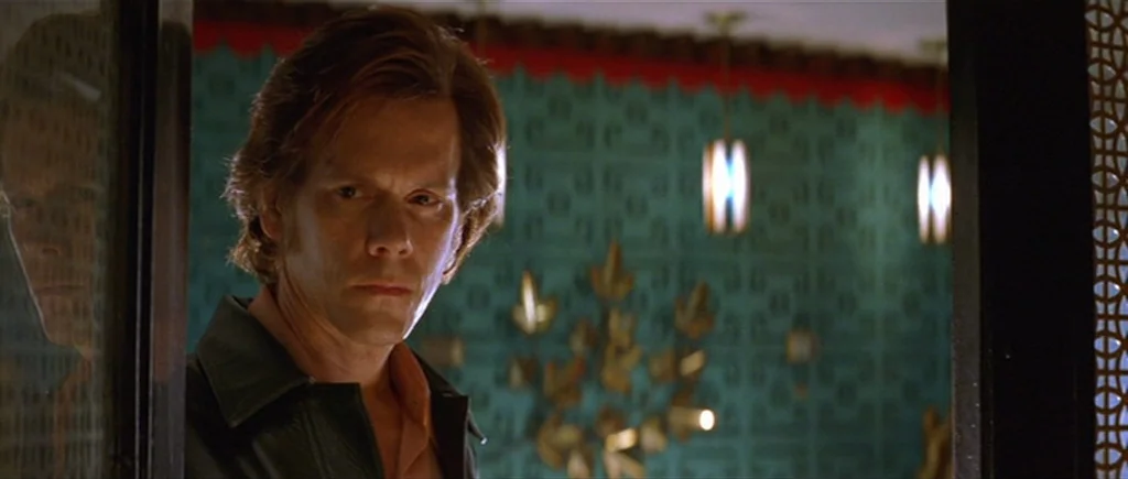 Where The Truth Lies (2005) movie still: medium — A man stands in a dark doorway with teal-patterned wallpaper visible behind him. The wall features…