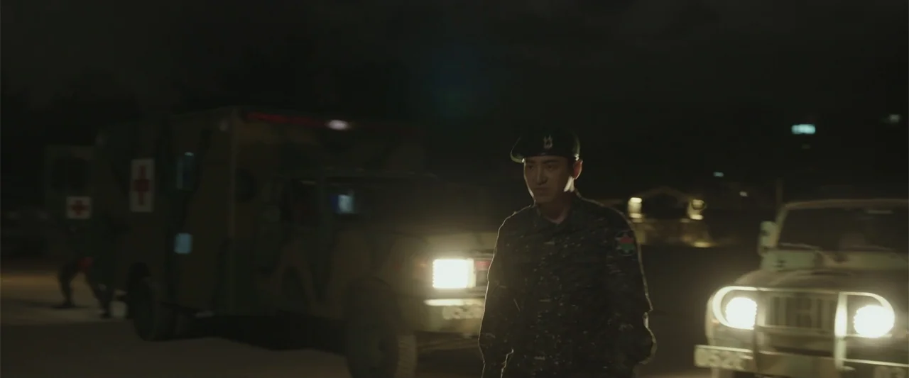 Along with the Gods: The Two Worlds (2017) movie still: medium — A military encampment at night features parked trucks and a soldier walking past.…