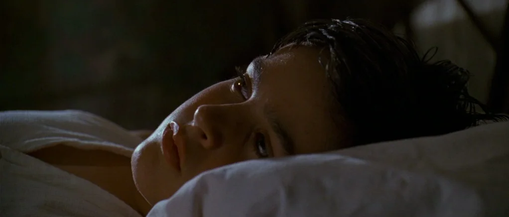 King of the Hill (1993) movie still: closeup — A dimly lit room at night features a person resting their head on a pillow. A young man lies with his…
