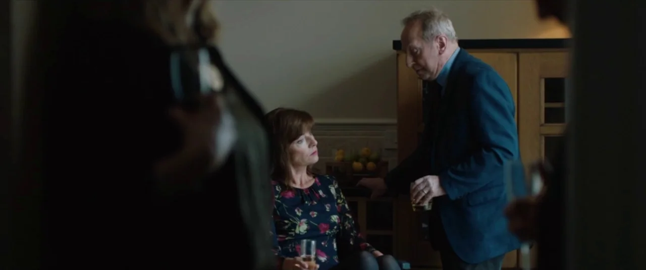 Happy New Year, Colin Burstead (2018) movie still: medium — A dimly lit indoor space with dark silhouettes framing a man and woman. The man stands…