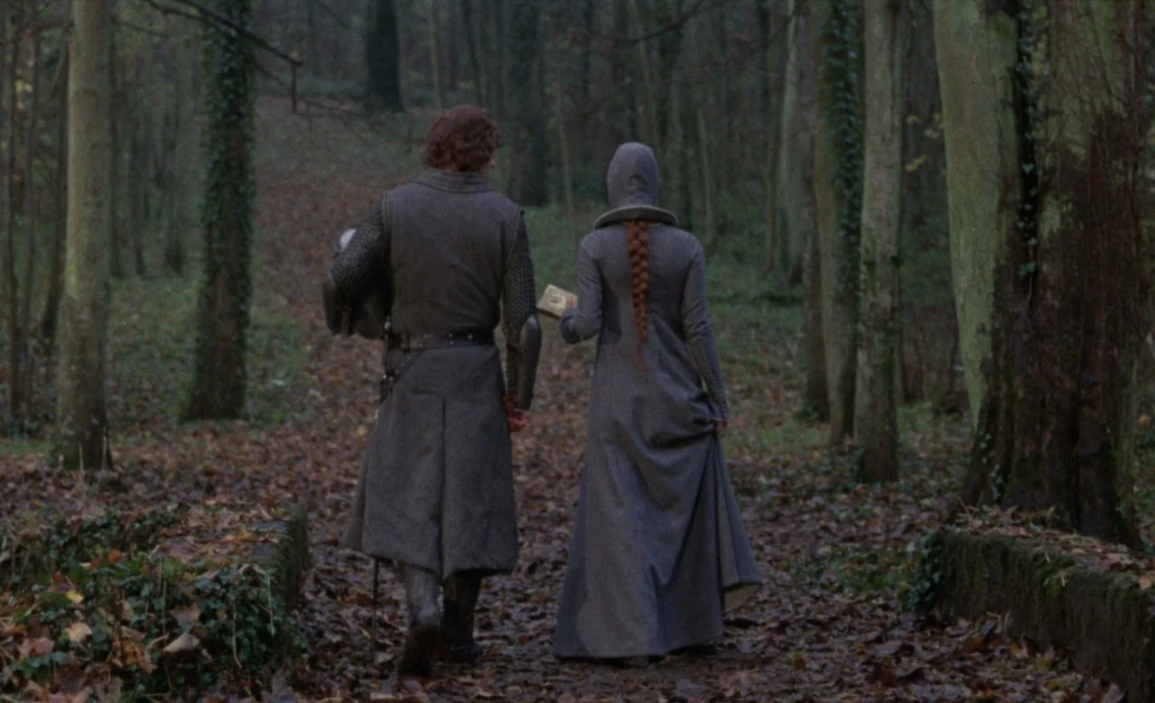 Blanche (1971) movie still: fullbody — A man in medieval armor and a woman in a grey dress walk away. They move along a narrow leaf-covered path…