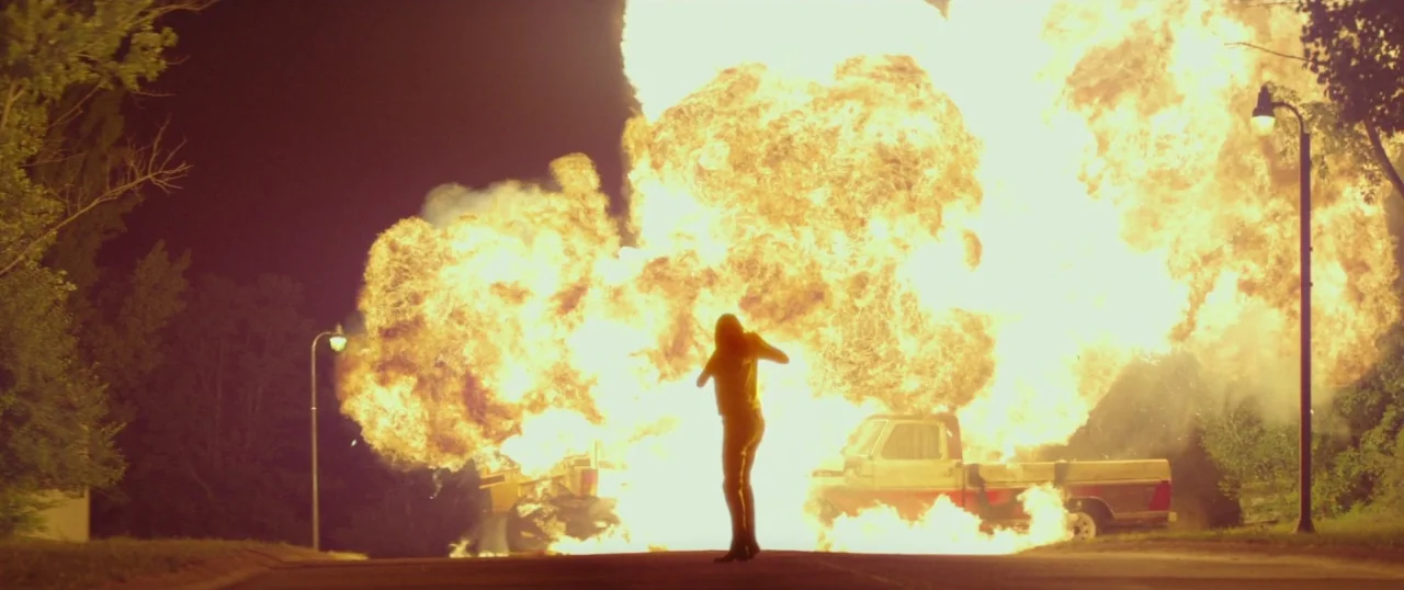 The Strangers: Prey at Night (2018) movie still: wide — An asphalt road at night features a large, bright orange fire explosion. A solitary figure…