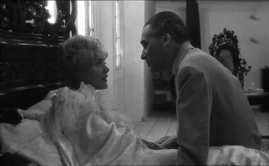 Cléo from 5 to 7 movie still: medium — A light-filled room features a carved wooden bedframe and a decorative mirror background. A woman sits…