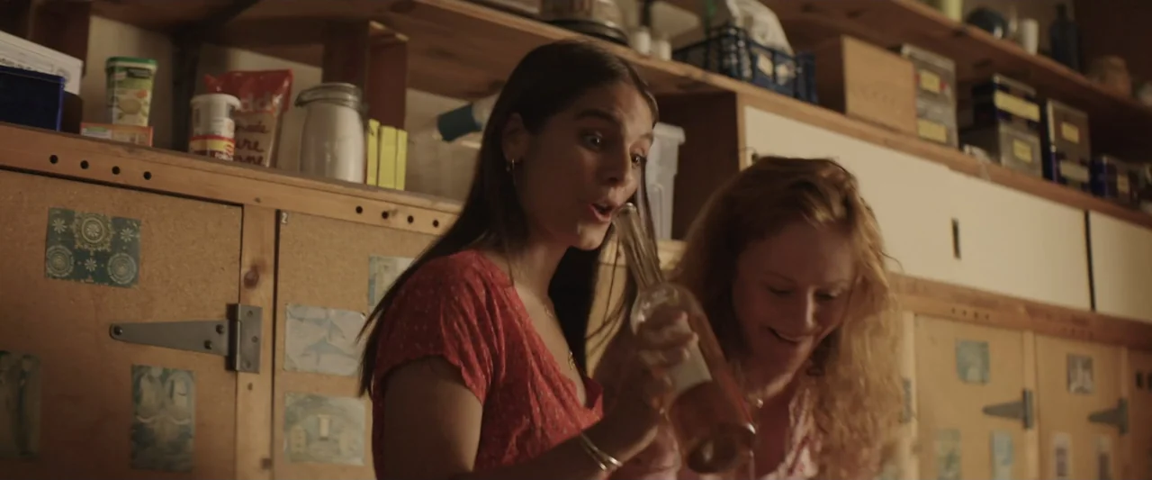 The Only One (2021) movie still: medium — A domestic kitchen with wooden cabinets and shelves filled with food containers. Two women stand in front…
