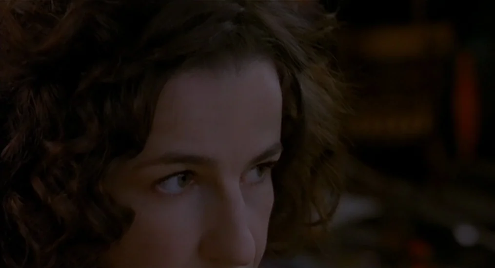 Vendredi Soir (2002) movie still: closeup — A dimly lit indoor space with shadows obscuring most of the background detail. A young woman with curly…