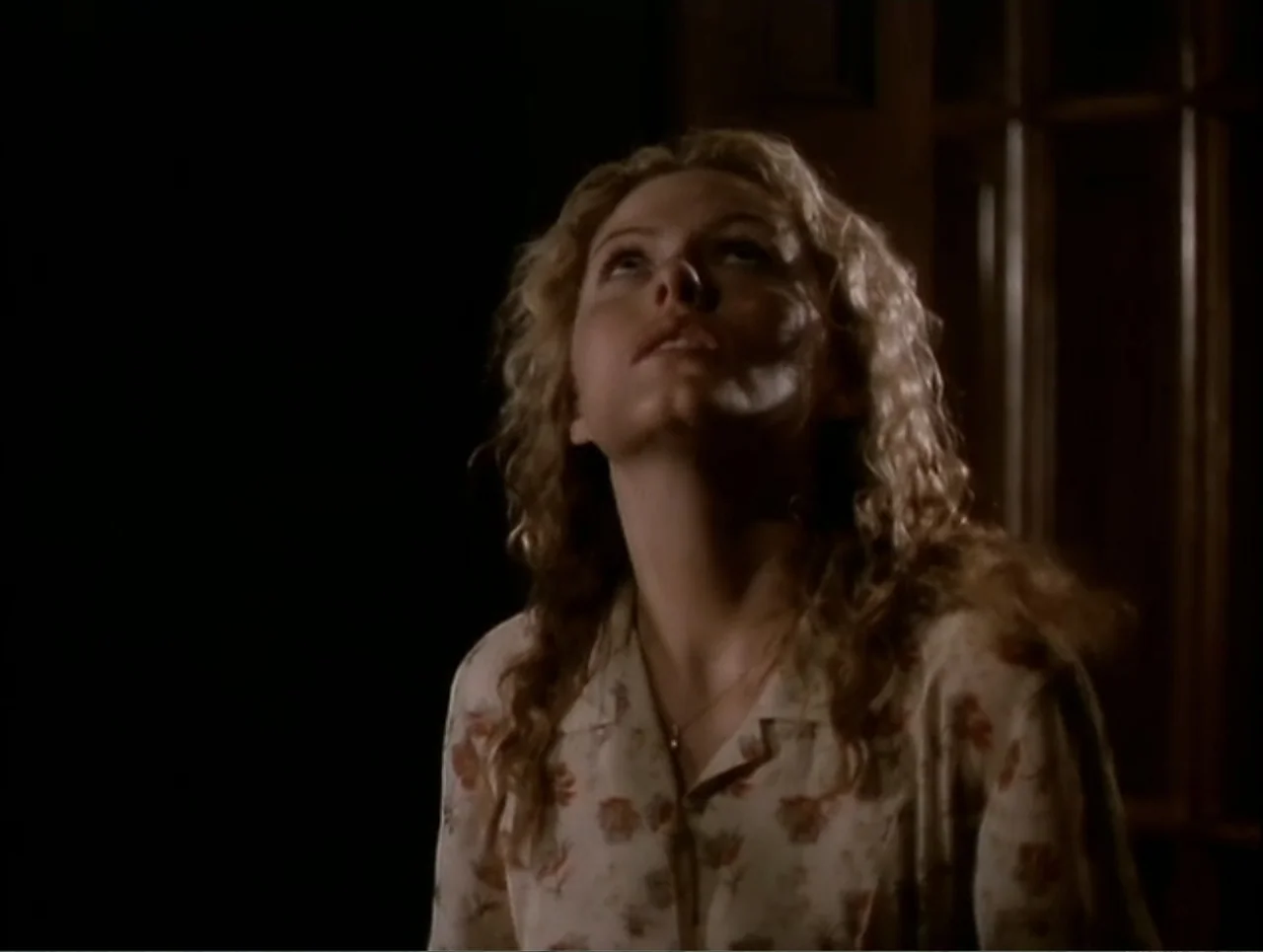 At the Midnight Hour (1995) movie still: medium — A dimly lit interior space features dark walls and a blurred wooden paneled door. A young woman…
