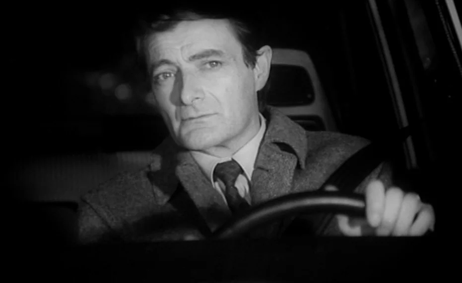 Vivement Dimanche (1983) movie still: medium — An interior of a vehicle during the night is dark and dimly lit. A middle-aged man in a wool coat…