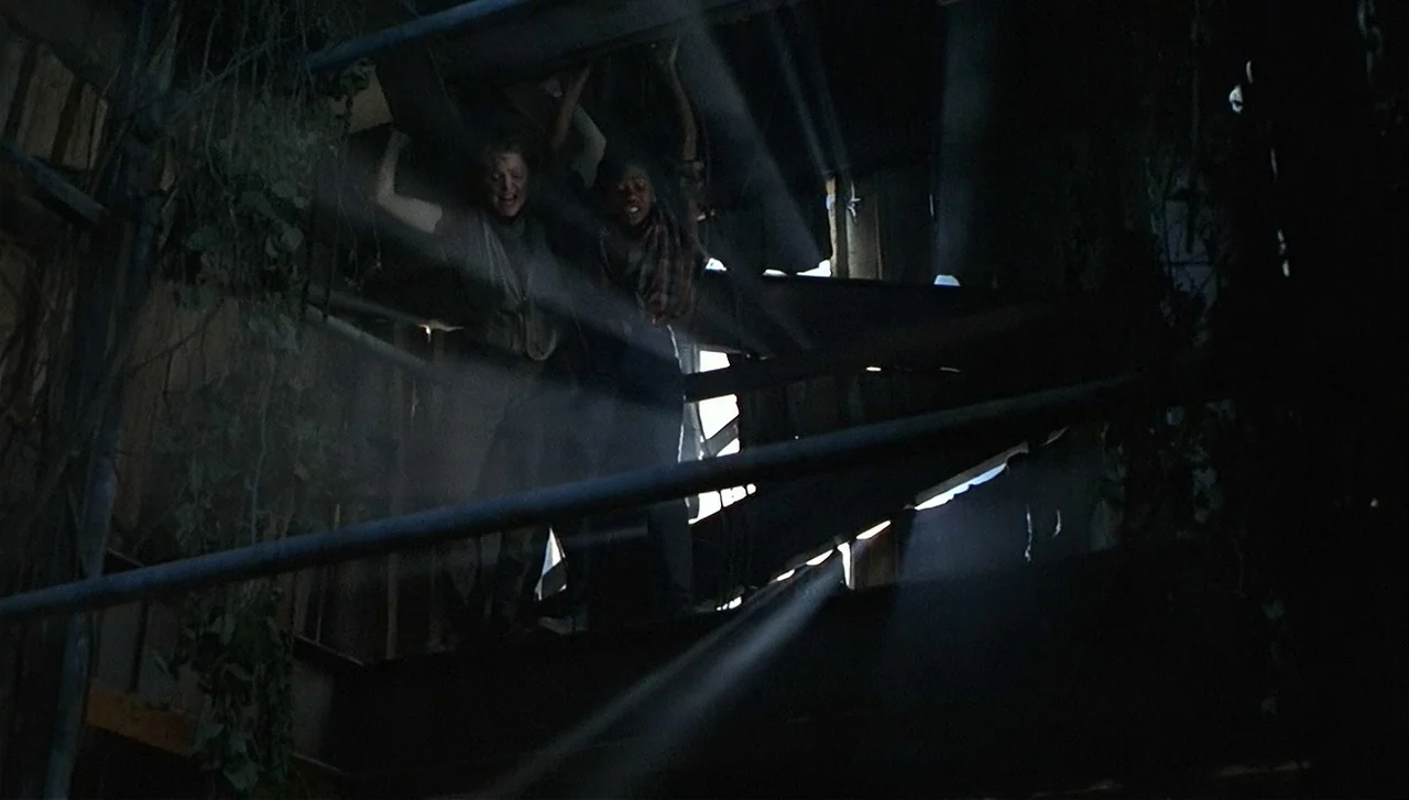 The Lost World: Jurassic Park (1997) movie still: medium — A dark, dilapidated interior with exposed metal beams and vines hanging from above. Two…