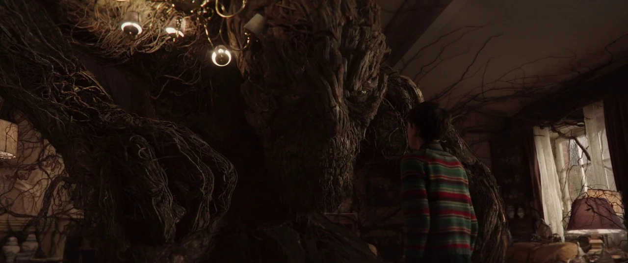 A Monster Calls (2016) movie still: medium — A dark, root-entangled interior space is filled with thick, textured wooden branches. A boy in a…