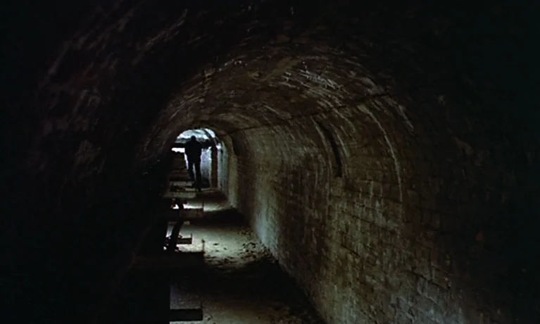 Nuits Rouges (1974) movie still: wide — A long, curved underground tunnel constructed from aged, stained bricks stretches into the distance. A…