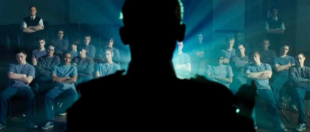 Hot Fuzz (2007) movie still: medium — A dark auditorium holds a group of young men seated in rows. A lecturer is seen from behind in silhouette as…