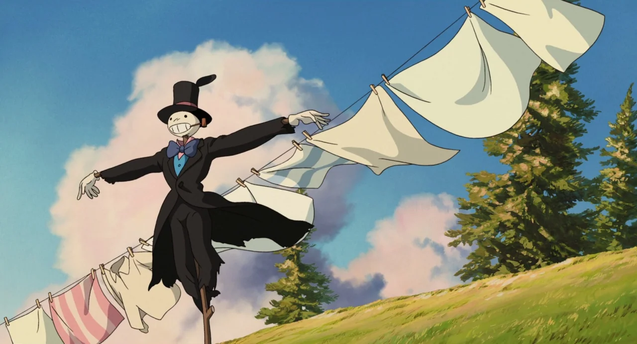 Howl’s Moving Castle (2004) movie still: medium — A green grassy hillside sits under a clear blue sky with large white clouds. A scarecrow wearing a…