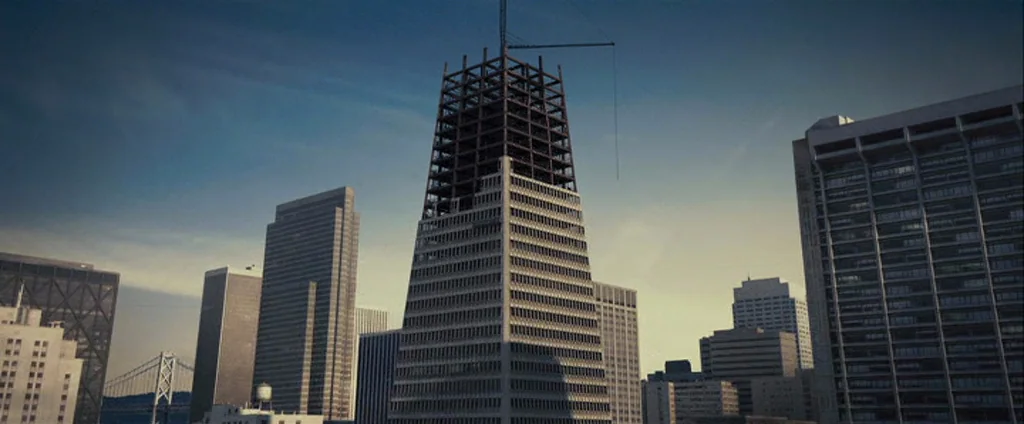 Zodiac (2007) movie still: establishing — An urban cityscape features a tapered skyscraper under construction with exposed steel framing at top.…