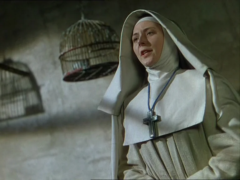 Black Narcissus (1947) movie still: medium — A plain stone room features two hanging birdcages against an off-white wall. A nun wearing a…