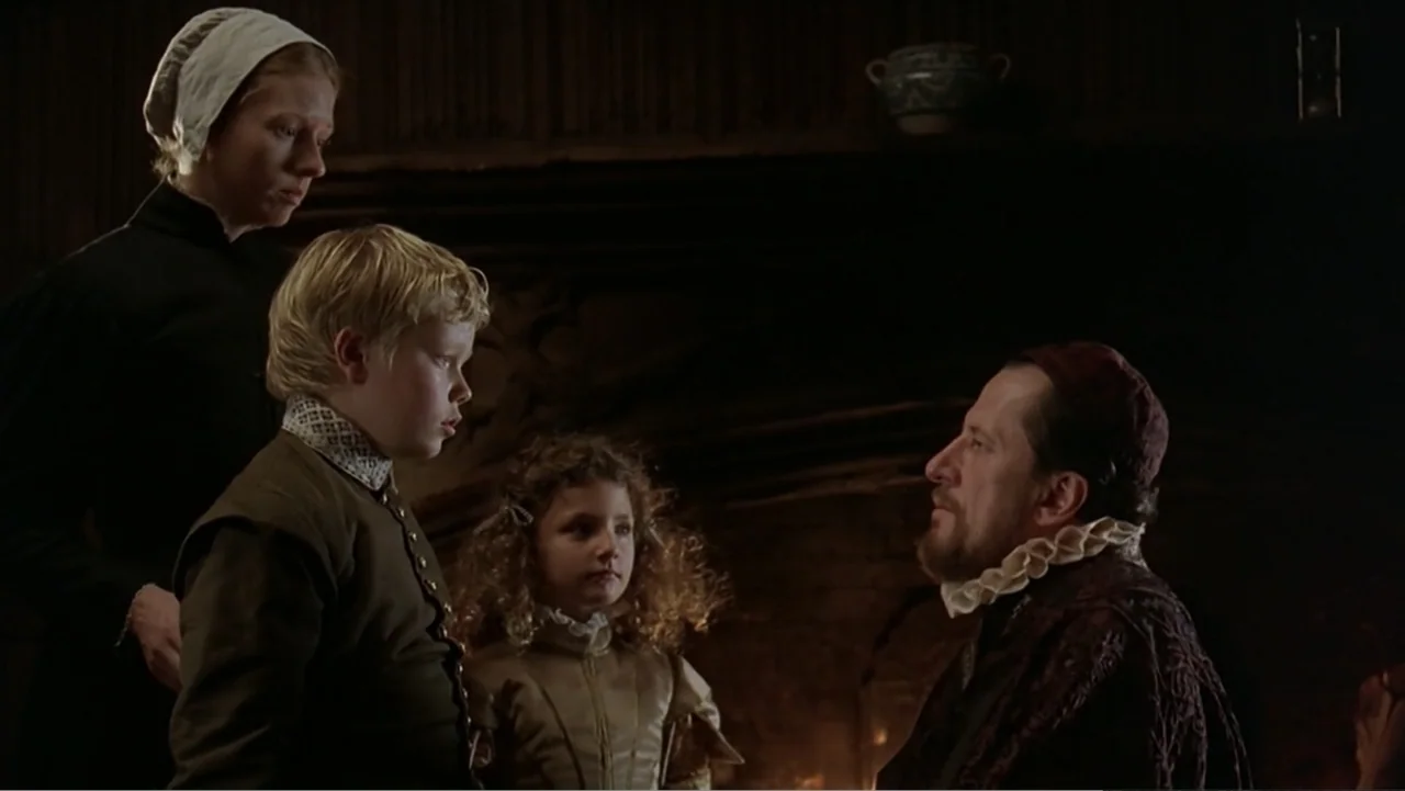 Elizabeth (1998) movie still: medium — A dimly lit room with dark wooden paneling featuring a large stone hearth. A man in period attire speaks to a…