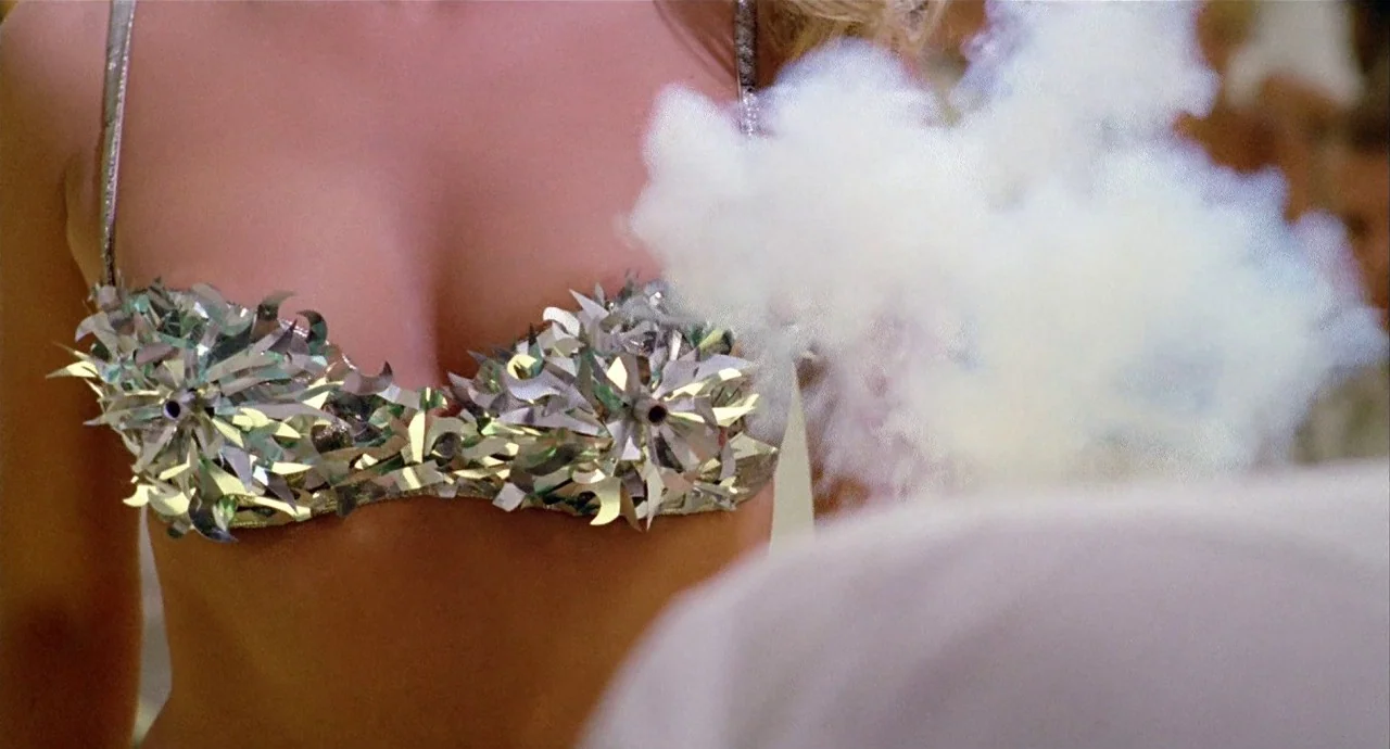 The 10th Victim (1965) movie still: closeup — A woman's torso wearing a custom metallic stage bra with active smoke emitters attached. Thick white…